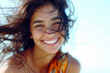A woman with tousled hair and a wide smile stands on a beach, bathed in sunlight