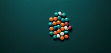  A Pile Of Pills Sitting On Top Of A Green Table Next To An Orange And White Pill Pill On Top Of A Green Table Next To An Orange And White Pill.