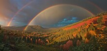  A Painting Of Two Rainbows In The Sky Over A Green Valley With Trees And A Mountain In The Distance With A Rainbow In The Sky And A Rainbow In The Middle Of The Sky.