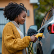 People charging battery in electric car. Young black woman holding charging cable plugged in electric vehicle.