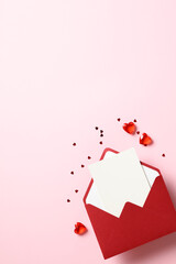 Wall Mural - Red paper envelope with blank white note mockup inside, red hearts and confetti on pastel pink background.