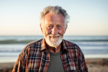 Wall Mural - Portrait of a tender man in his 80s dressed in a relaxed flannel shirt against a sandy beach background. AI Generation