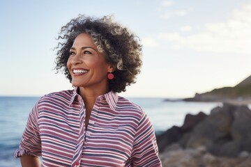 Wall Mural - Portrait of a cheerful afro-american woman in her 60s donning a classy polo shirt against a rocky shoreline background. AI Generation