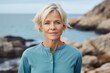 © CogniLens - Portrait of a content woman in her 60s wearing a sporty polo shirt against a rocky shoreline background. AI Generation