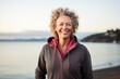 Portrait of a smiling woman in her 50s wearing a zip-up fleece hoodie against a calm bay background. AI Generation