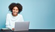© Danko - Young african american woman smiling sitting with laptop isolated on blue background