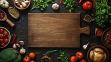 Empty Wooden Chopping Board Surrounded By Fresh Vegetables, Herbs, Spices, Olive Oil, And Cooking Utensils On A Dark Table.