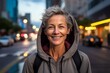 Portrait of a grinning woman in her 50s sporting a comfortable hoodie against a bustling city street background. AI Generation