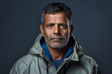 Wall Mural - Portrait of a tender indian man in his 50s wearing a lightweight packable anorak against a minimalist or empty room background. AI Generation