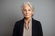 Portrait of a tender woman in her 70s wearing a professional suit jacket against a light wood minimalistic setup. AI Generation