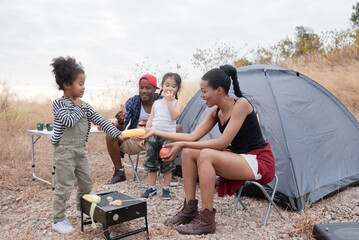 Happy African American family with adorable children enjoy weekend vacation camping outdoors in countryside, cheerful children laughing running around father holding apple fruit, bonding relationship