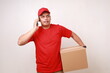 © ArvStd - Happy Asian courier man in red holding a cardboard box while talking on the phone. Isolated on white
