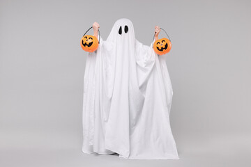 Wall Mural - Child in white ghost costume holding pumpkin buckets on light grey background. Halloween celebration