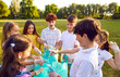 © Studio Romantic - Group of a young teenage happy smiling volunteers children standing in a row in gloves and with garbage bags collecting trash in the summer park outdoors. Cleaning environmental pollution by garbage.