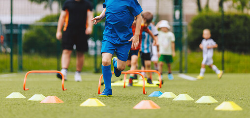 Wall Mural - Group of children on physical education training with coach. Sport school training for elementary age class. Sporty kids jumping over hurdles on the training field