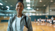 © Studio Nova - female coach holding a clipboard is standing in a gymnasium with a group of students seated on the floor in the background