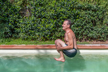  Caucasian man with a funny expression takes a bomb dive in the swimming pool on a sunny day	