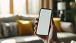 © Studio Nova - Hand is holding a smartphone with a blank screen in a room with a blurred background featuring modern interior elements.