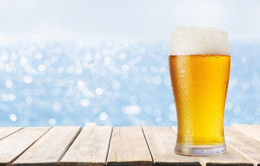 Wall Mural - glass of beer on wooden table on sea background