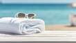 Coastal essentials: White towel and sunglasses on a wooden table at the beach.