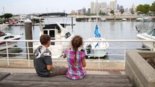 Brother And Sister Sitting On A Bench Near The Moored Boats