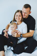 © DSMT - Young mother and father play with their newborn son lying in a white bed. A stylish family with a small child
