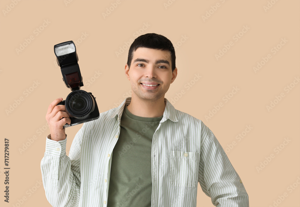 Young male photographer with professional camera on beige background