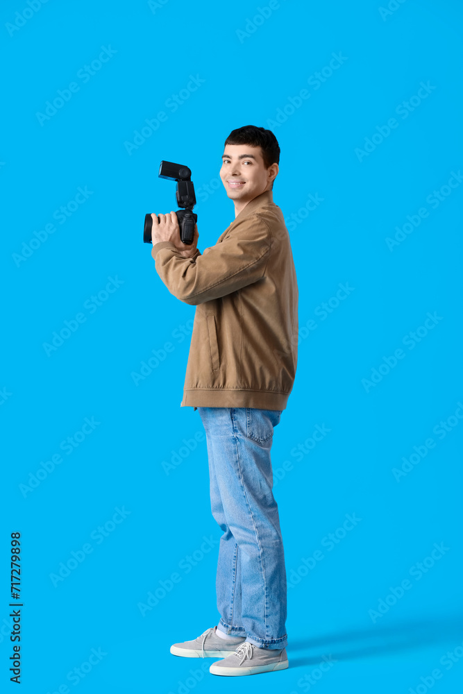 Young male photographer with professional camera on blue background