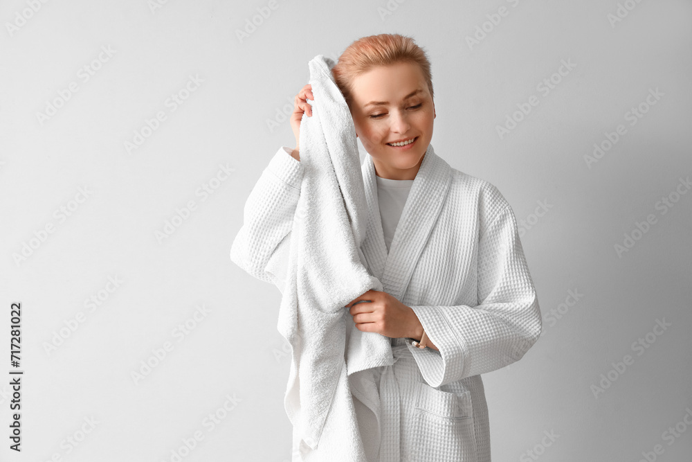 Young woman in bathrobe with towel on light background