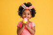 © Анастасия Бутко - Happy african american girl with bunny ears holding colored Easter egg against yellow background