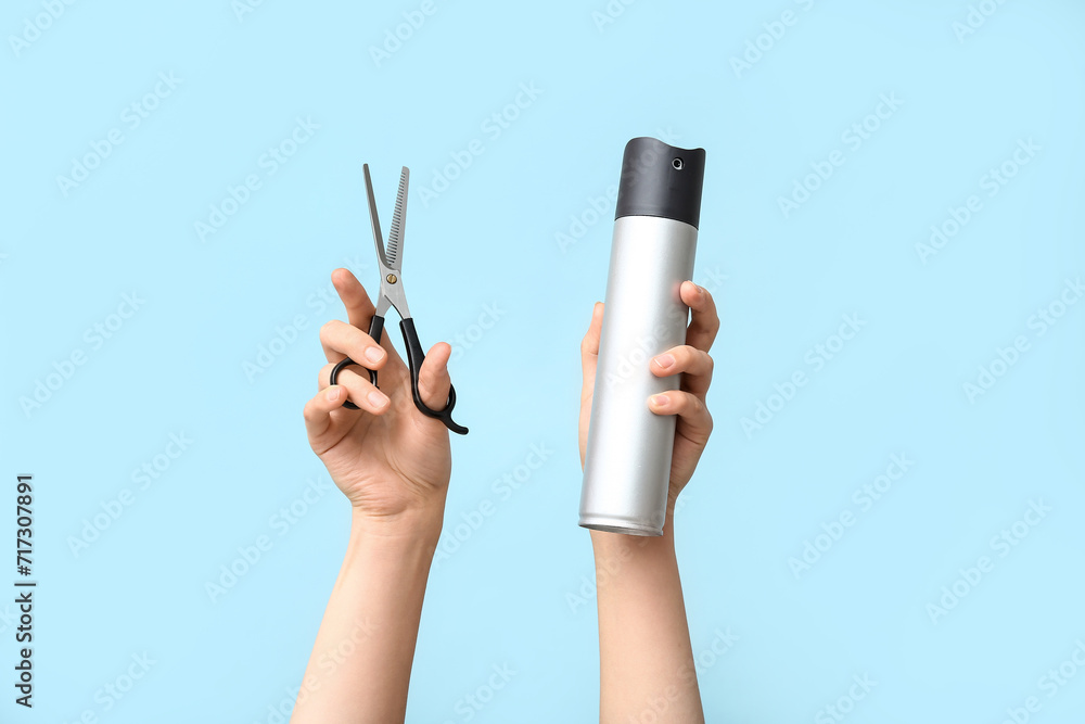 Female hands with scissors and hairspray on color background.