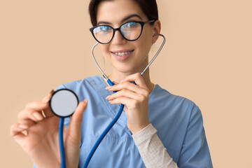 Canvas Print - Female medical intern with stethoscope on beige background, closeup