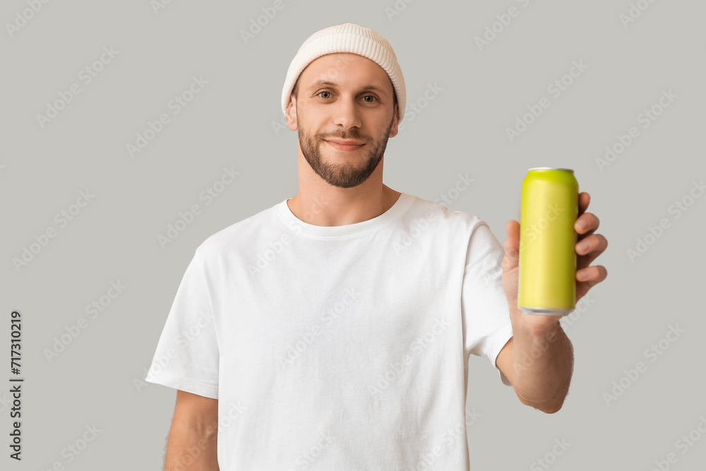 Young man with can of cold beer on grey background