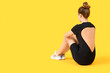 © Pixel-Shot - Young woman in cycling jumpsuit sitting on yellow background, back view