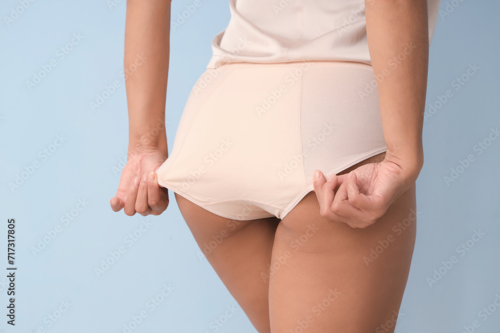 Young woman in menstrual panties on blue background, back view
