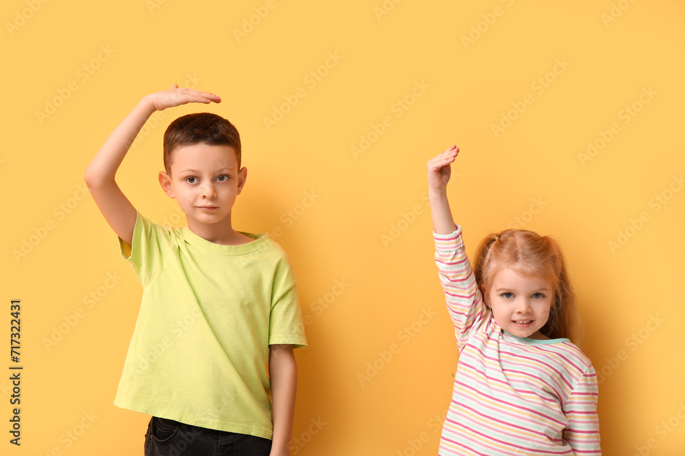 Cute little children measuring height on yellow background