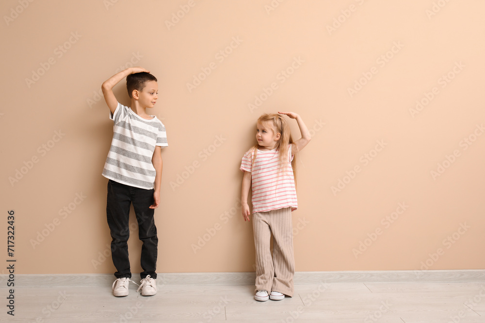 Cute little children measuring height near beige wall