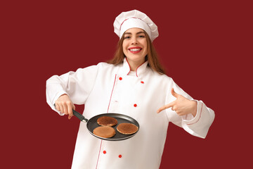 Sticker - Happy young female chef pointing at frying pan with tasty pancakes on red background