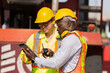 © amorn - Group of diverse male container yard worker working and checking container boxes at commercial dock site. Black male and Asian male people worker inspecting container boxes from cargo freight ship