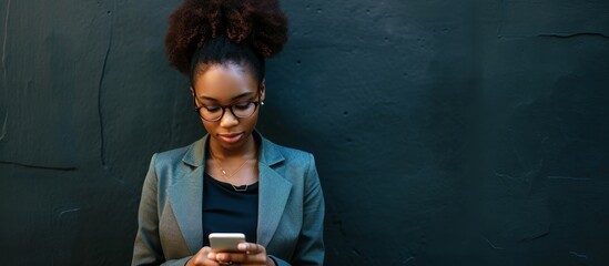 Sticker - A black young adult businesswoman is outside, using her cellphone beside a dark wall and with her back to the camera.