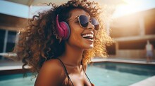 Girl in trendy sunglasses walking by swimming pool outside. Funny cheerful young woman in headphones enjoying music. Happy woman concept.