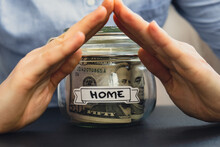 Unrecognizable Woman Holding Saving Money In Glass Jar Filled With Dollars Banknotes. HOME Transcription In Front Of Jar. Managing Personal Finances Extra Income For Future Insecurity