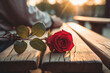 A Red rose flower on a wooden table. A person waiting for his or her partner in the blurred background. Concept of love and care