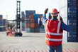 back view African factory worker or engineer using walkie talkie and showing stop gesture to crane car in containers warehouse storage