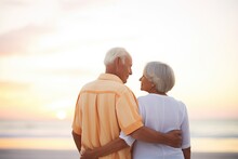 Retired Couple Watching Sunset Arm In Arm On A Beach
