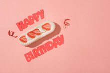 Top View Of The Red HAPPY BIRTHDAY Text And Decorative Ribbon Around A Cake On A Pink Background. Free Space For Display And Text Design. Copy Space.