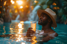 Young Black Afro American Man Hotel Guest Sipping A Cocktail In The Outdoor Hotel Swimming Pool During Summer Holidays