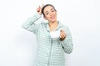 Funny Beautiful young woman wearing green plaid pyjama and holding a cup shows horns, fingers on head gesture, posing silly and cute
