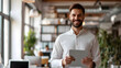 © SS Digital - A happy young businessman at work, clutching a pad computer in his hands. A fintech tablet device is being used by a male professional employee who is standing in the office and reviewing financial ma