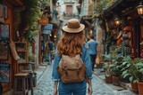 Fototapeta Uliczki - Summer Vibes: A Woman in a Tan Hat and Jean Jacket Carries a Backpack Down a Cobblestone Street Generative AI